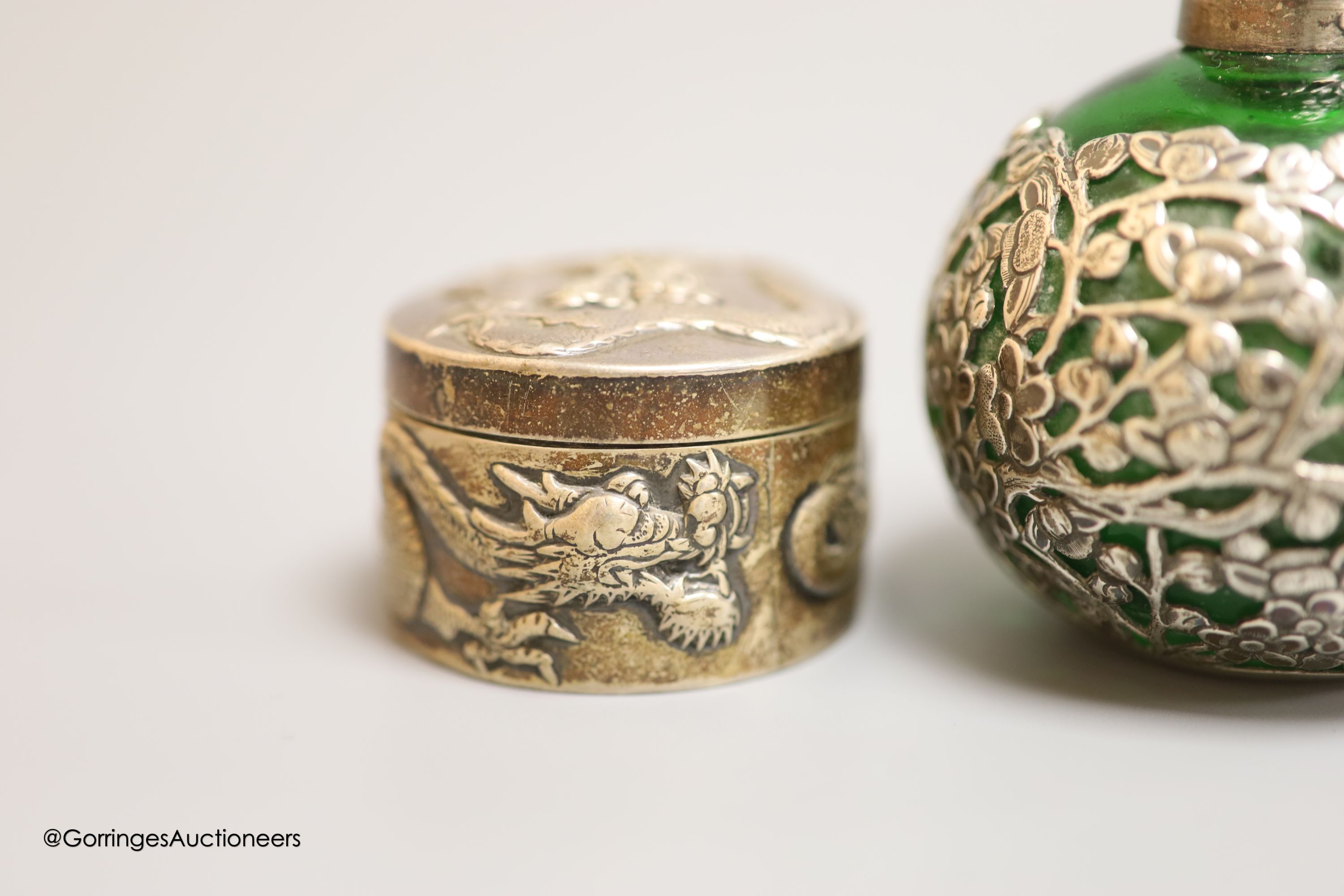 A late 19th/early 20th century Chinese Export white metal circular box, by Wang Hing, embossed with dragons, diameter 5cm, together with a similar white metal overlaid green glass scent flask by Wang Hing, height 11.6cm.